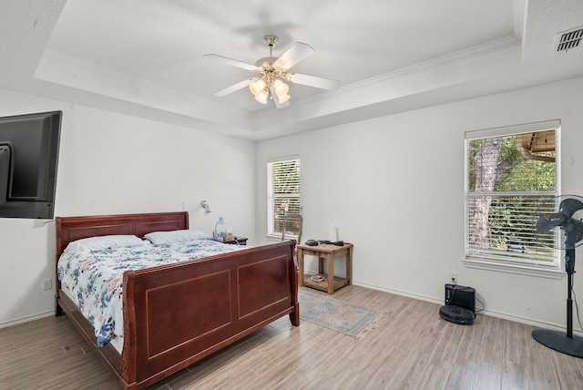 bedroom featuring a raised ceiling, wood finished floors, visible vents, and baseboards