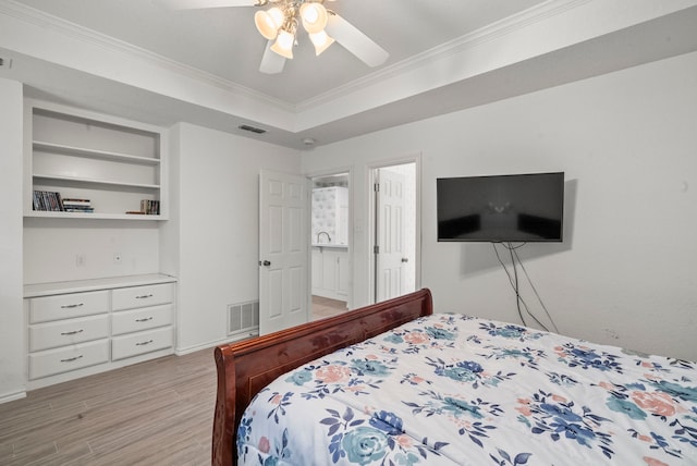 bedroom with a raised ceiling, crown molding, visible vents, and light wood finished floors