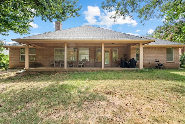 back of property featuring a yard, a patio, brick siding, and a chimney