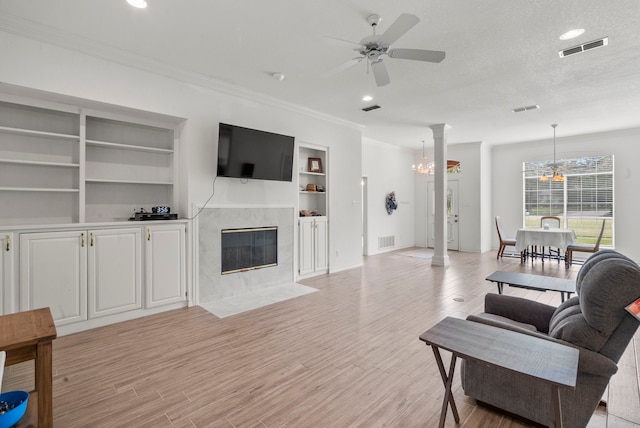 living area featuring light wood-type flooring, visible vents, a high end fireplace, and ceiling fan with notable chandelier