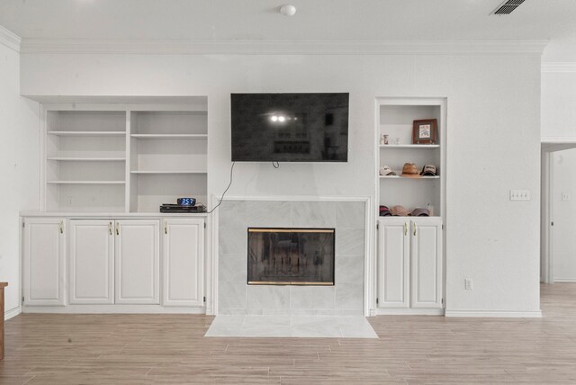 unfurnished living room with light hardwood / wood-style flooring, built in features, a tiled fireplace, and ornamental molding