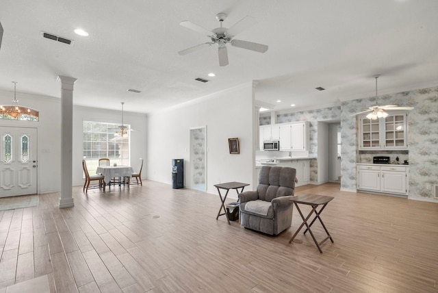 interior space with visible vents, ceiling fan, ornamental molding, light wood-style flooring, and ornate columns