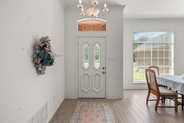 foyer with light wood-type flooring, visible vents, a chandelier, and crown molding