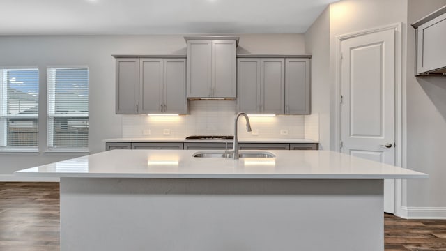 kitchen with sink, gray cabinets, dark wood-type flooring, decorative backsplash, and a center island with sink