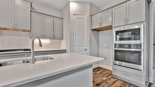 kitchen featuring gray cabinets, sink, decorative backsplash, dark hardwood / wood-style floors, and appliances with stainless steel finishes