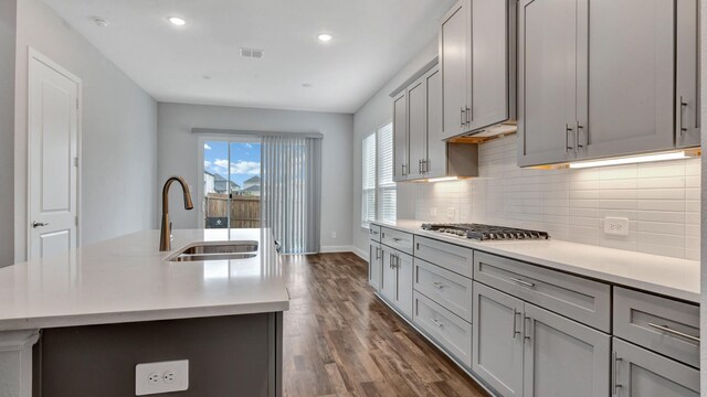 kitchen with gray cabinetry, dark hardwood / wood-style floors, backsplash, a kitchen island with sink, and sink