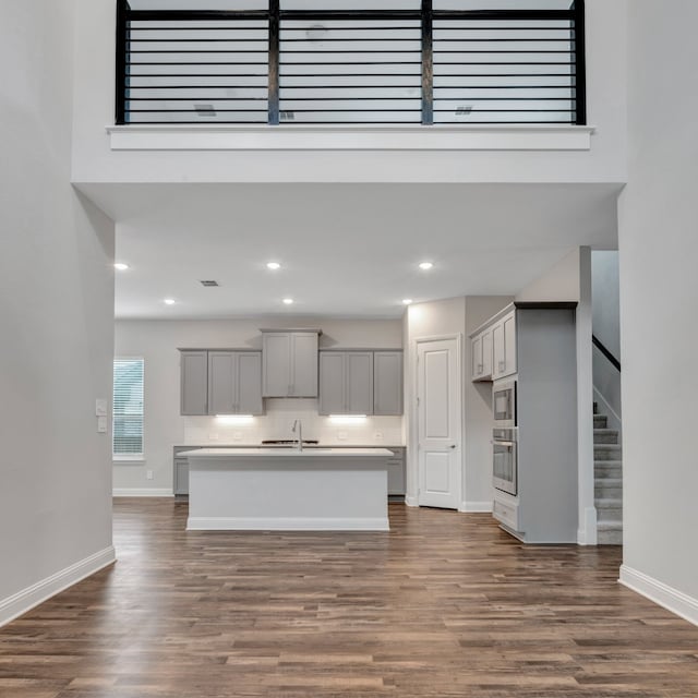 kitchen with appliances with stainless steel finishes, a kitchen island with sink, sink, dark hardwood / wood-style floors, and tasteful backsplash