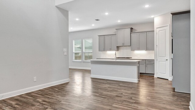 kitchen featuring gray cabinetry, backsplash, dark hardwood / wood-style flooring, and an island with sink