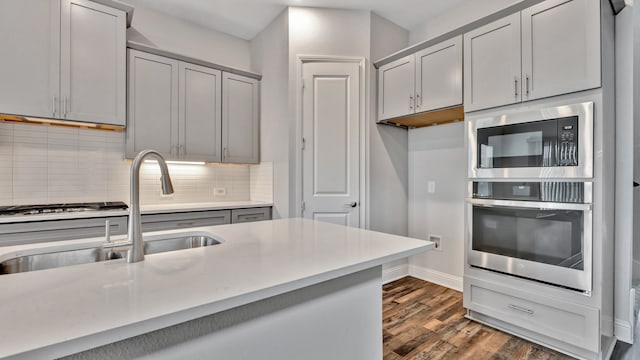 kitchen with gray cabinetry, backsplash, appliances with stainless steel finishes, dark hardwood / wood-style flooring, and sink