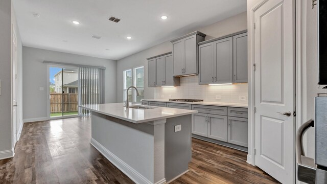 kitchen with gray cabinetry, stainless steel gas stovetop, dark hardwood / wood-style floors, and a kitchen island with sink