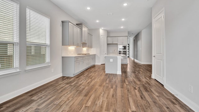 kitchen with black microwave, tasteful backsplash, dark hardwood / wood-style flooring, and a kitchen island with sink