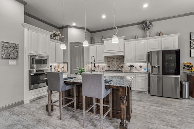 kitchen with light stone countertops, stainless steel appliances, a kitchen island with sink, white cabinets, and light wood-type flooring