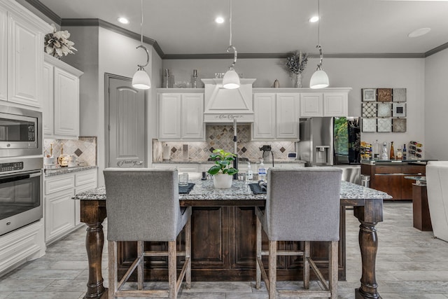 kitchen with a center island with sink, hanging light fixtures, appliances with stainless steel finishes, and light stone counters