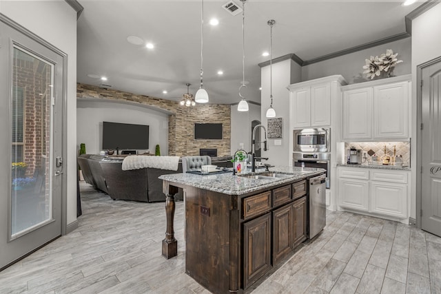 kitchen with a fireplace, stainless steel appliances, sink, white cabinets, and hanging light fixtures