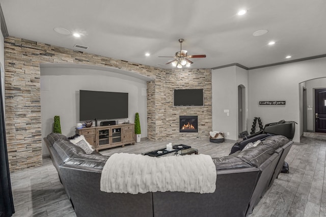 living room with a fireplace, ceiling fan, crown molding, and light wood-type flooring