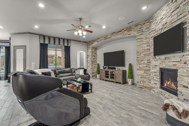 living room featuring ceiling fan, light hardwood / wood-style floors, and a stone fireplace