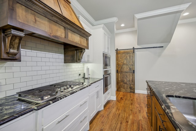 kitchen with custom range hood, wood-type flooring, stainless steel appliances, white cabinetry, and a barn door