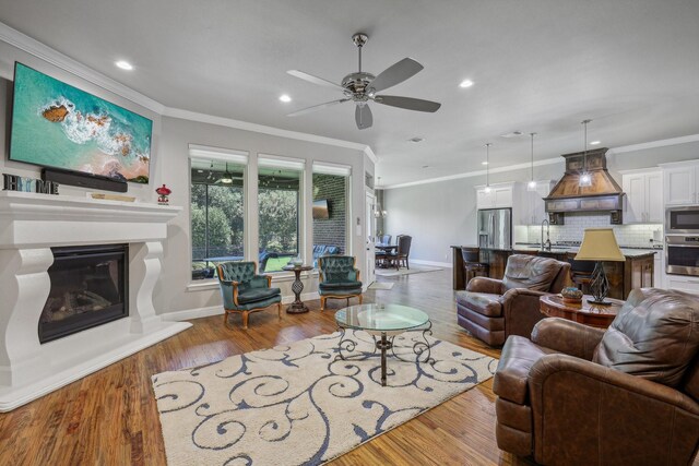 living room with crown molding, hardwood / wood-style flooring, sink, and ceiling fan