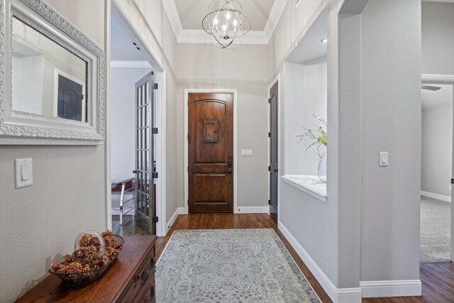 entrance foyer with dark wood-type flooring, an inviting chandelier, and ornamental molding