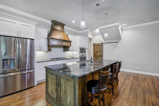 kitchen with stainless steel appliances, a barn door, an island with sink, custom range hood, and white cabinets