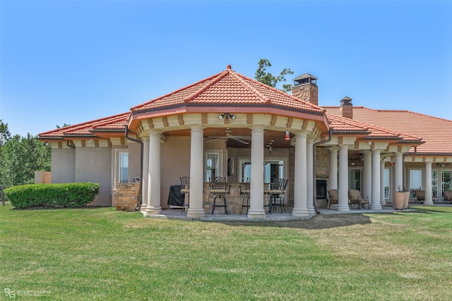 back of house featuring a lawn, ceiling fan, and a bar