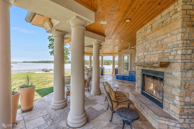 view of patio with ceiling fan, a water view, and an outdoor stone fireplace