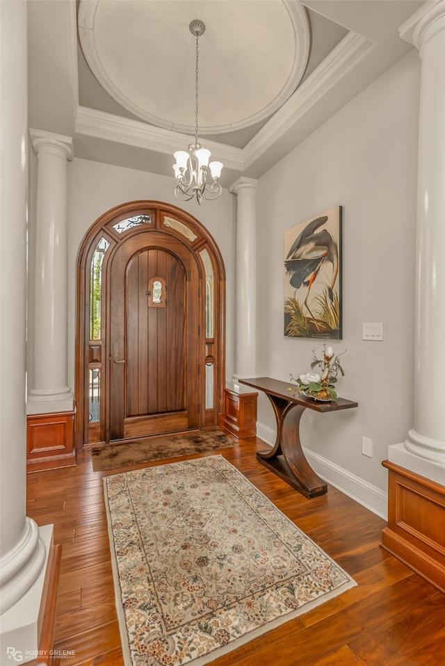 entrance foyer with crown molding, ornate columns, a tray ceiling, dark hardwood / wood-style flooring, and a chandelier