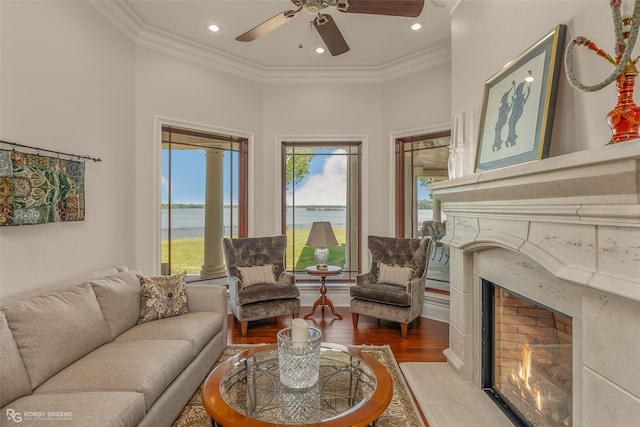 living room with a high end fireplace, crown molding, a water view, and hardwood / wood-style flooring