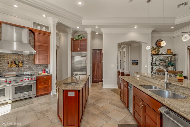 kitchen with sink, light stone counters, high quality appliances, and wall chimney range hood