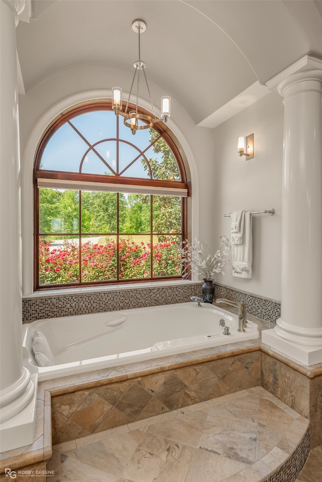 bathroom featuring tiled tub, decorative columns, a wealth of natural light, and an inviting chandelier