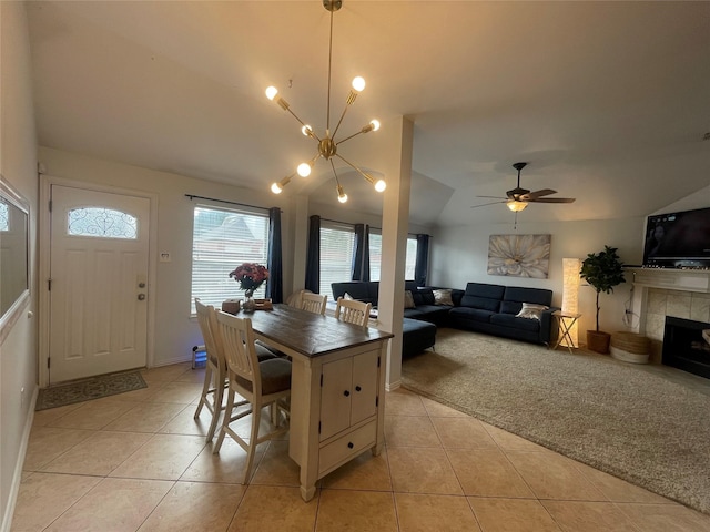 carpeted dining space with ceiling fan with notable chandelier, a tile fireplace, and vaulted ceiling