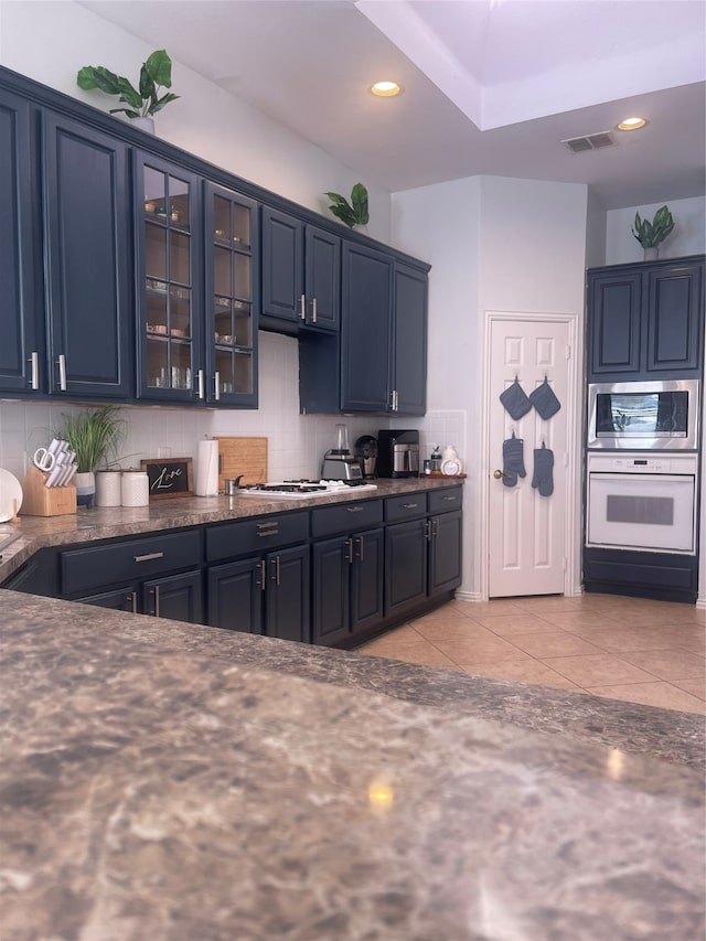 kitchen featuring white gas stovetop, blue cabinetry, light tile patterned floors, tasteful backsplash, and dark stone countertops