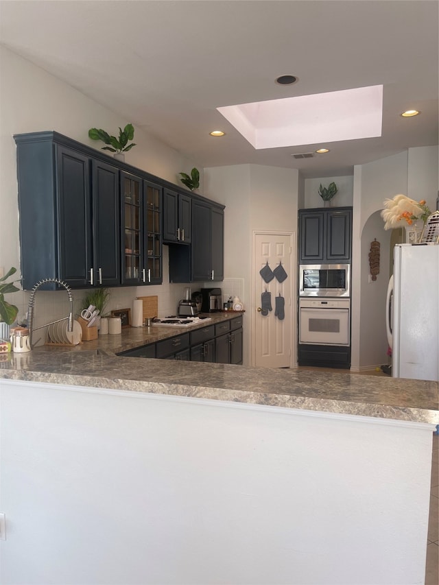 kitchen with kitchen peninsula, sink, white appliances, and a tray ceiling