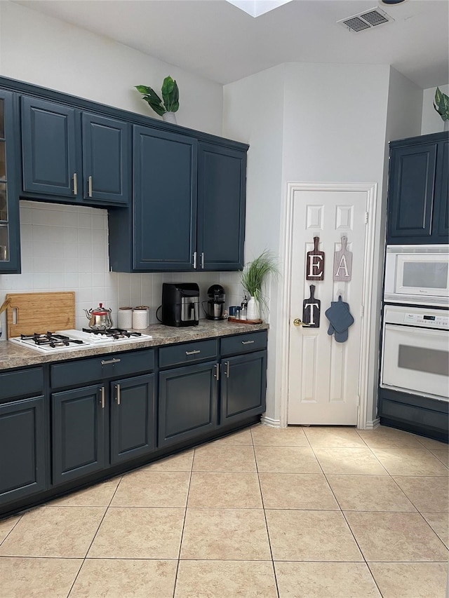 kitchen featuring backsplash, blue cabinetry, light tile patterned floors, and white appliances