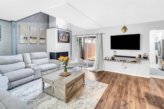 living room with a multi sided fireplace, brick wall, and dark wood-type flooring