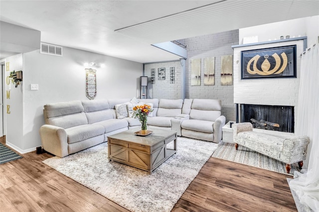 living room with wood-type flooring, a fireplace, and brick wall