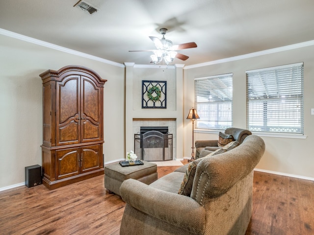 living room featuring ceiling fan, hardwood / wood-style flooring, a tiled fireplace, and ornamental molding