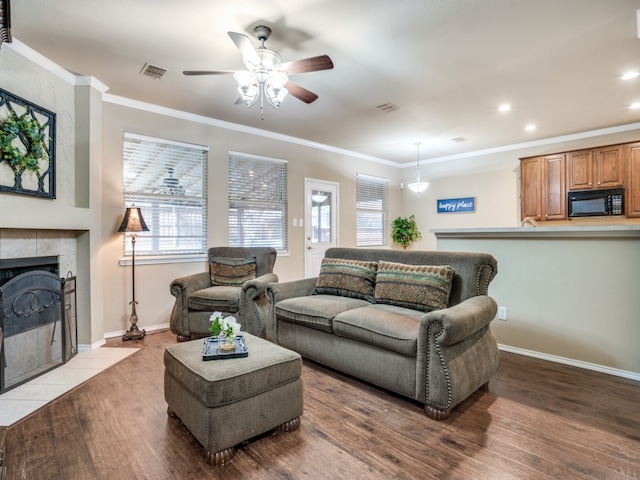 living room with dark hardwood / wood-style floors, crown molding, ceiling fan, and a tile fireplace