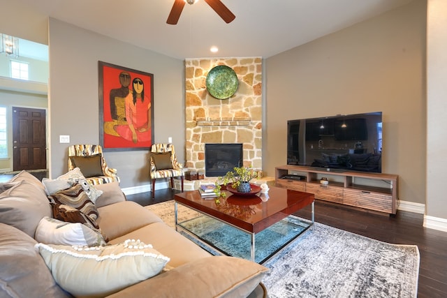 living room featuring dark wood-type flooring, ceiling fan, and a stone fireplace