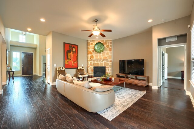 living room with ceiling fan, dark hardwood / wood-style flooring, and a stone fireplace