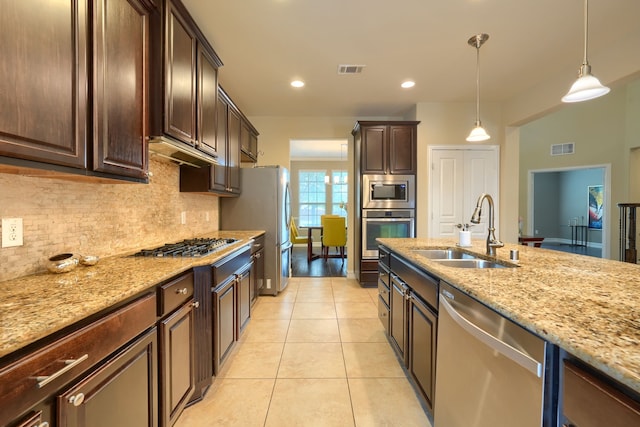 kitchen featuring appliances with stainless steel finishes, light stone counters, sink, pendant lighting, and dark brown cabinetry