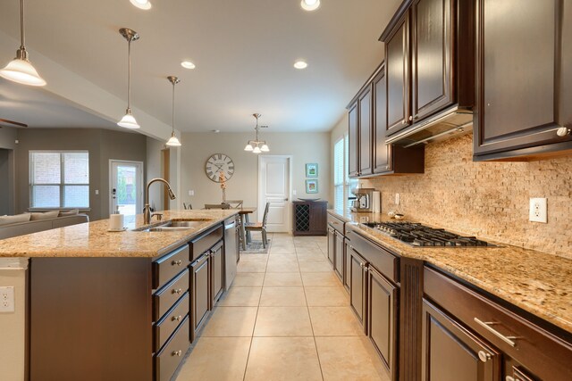 kitchen featuring a kitchen island with sink, sink, light stone countertops, hanging light fixtures, and appliances with stainless steel finishes