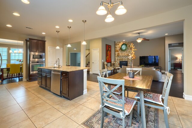 interior space with pendant lighting, stainless steel appliances, ceiling fan with notable chandelier, and a stone fireplace