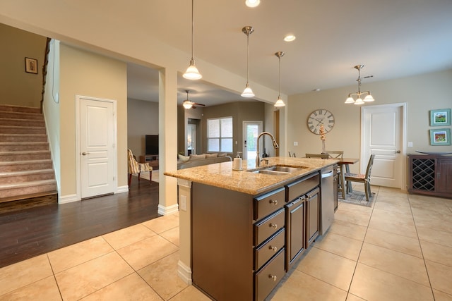 kitchen featuring ceiling fan with notable chandelier, decorative light fixtures, light stone counters, sink, and a center island with sink