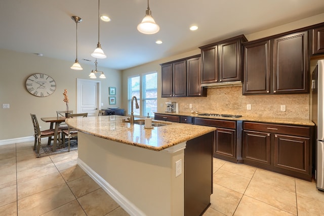 kitchen featuring dark brown cabinets, sink, light stone countertops, hanging light fixtures, and a center island with sink