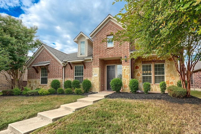 traditional-style house with a front yard, stone siding, brick siding, and roof with shingles