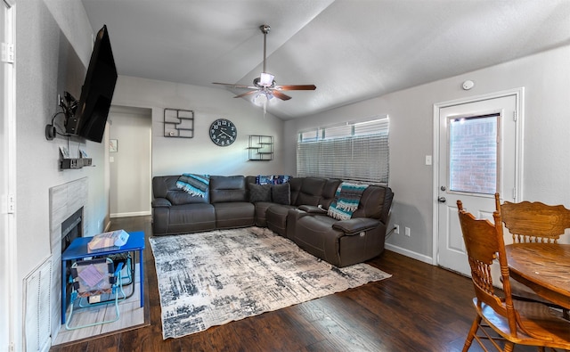 living room featuring dark hardwood / wood-style floors, vaulted ceiling, ceiling fan, and a tiled fireplace