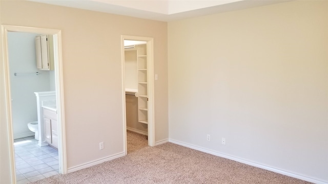 unfurnished bedroom with a closet, ensuite bath, a walk in closet, and light carpet