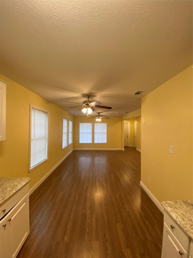 unfurnished living room featuring dark wood-type flooring, ceiling fan, and a textured ceiling