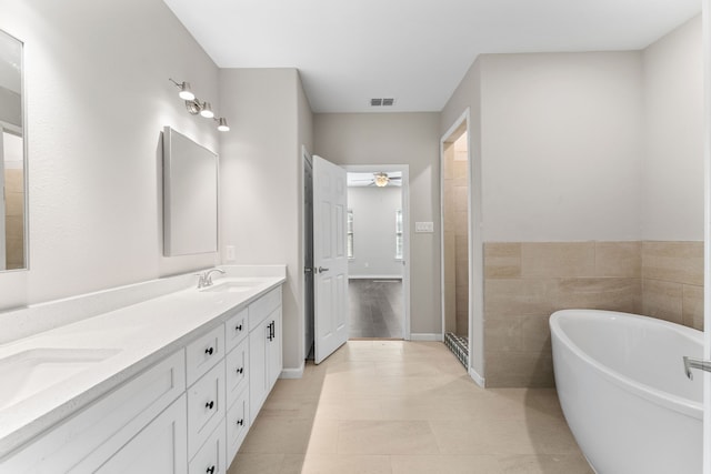 bathroom with ceiling fan, vanity, a bathtub, and tile walls